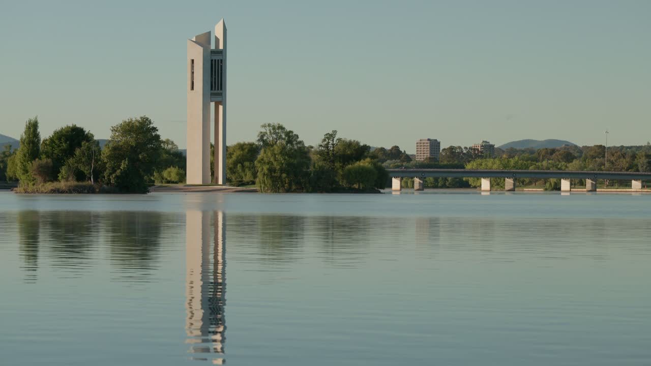 The National Carillon rises above Lake Burley Griffin, its reflection perfectly mirrored in the still water. The morning light enhances the beauty of this iconic Canberra landmark.