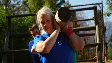 group of fit women carrying a heavy wooden log during obstacle course