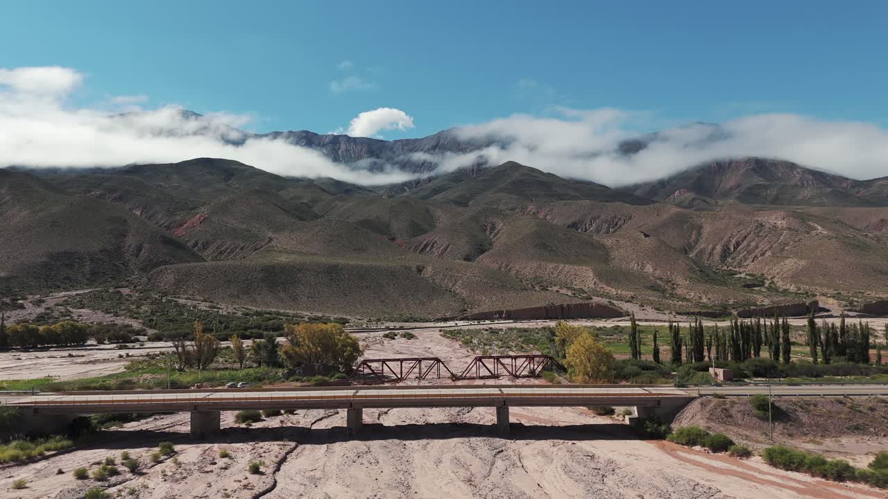 río seco con un pequeño puente, vuelo de avión no tripulado hacia las montañas nubladas en la provincia de jujuy en argentina, copia espacio y cámara lenta