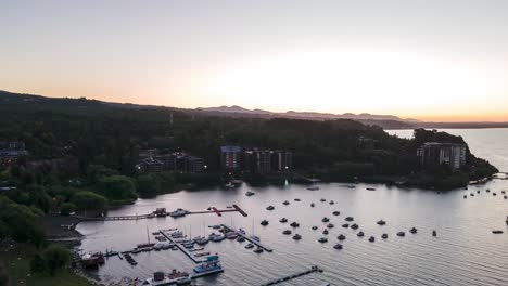 orbit hyperlapse of boats sailing in lake near docks on green hillside, villarrica volcano in background at sunset, la poza, pucon, chile
