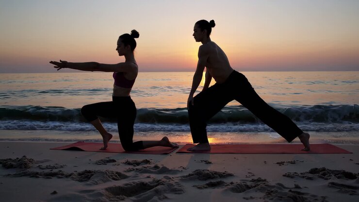 Couple practicing yoga on the beach at sunrise