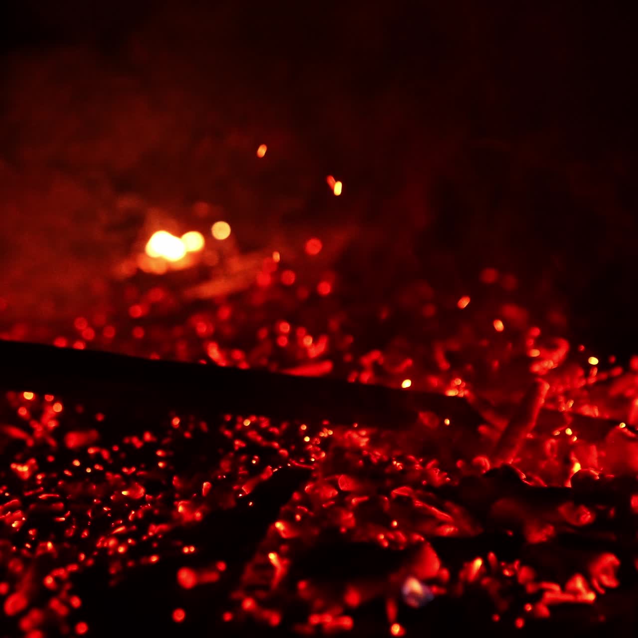 Hot smoldering red embers are moved by the stick. Bright sparkles flying up in the air. Black backdrop
