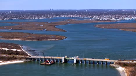 An-aerial-time-lapse-over-a-creek-on-Long-Island-New-York-with-a-bridge-for-vehicles-under-repair-on-a-sunny-day