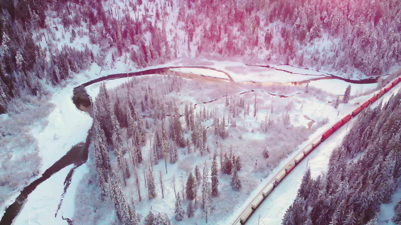 Train With Cargo Travelling By Snowy Forest With Coniferous Trees Covered With Snow In Winter At Glacier National Park. - aerial