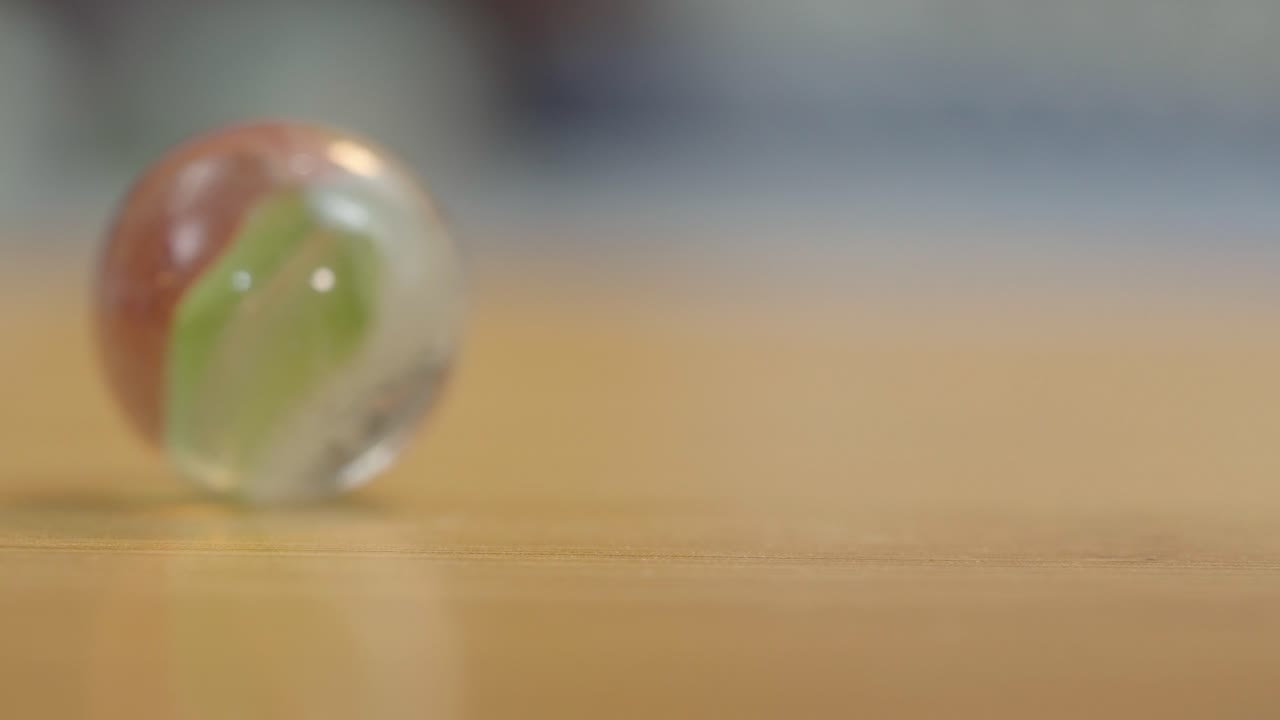 Close up macro view of glass marbles rolling on wooden surface with soft focus background, childhood memories and playtime