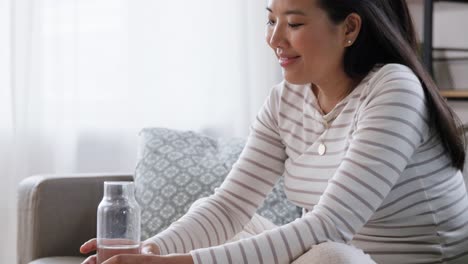 Mujer-Embarazada-Con-Agua-En-Botella-De-Vidrio-En-Casa.-Concepto-De-Embarazo,-Descanso,-Personas-Y-Expectativas.-Feliz-Sonriente-Mujer-Embarazada-Asiática-Sentada-En-Un-Sofá-En-Casa-Y-Bebiendo-Agua-De-Una-Botella-De-Vidrio-Reutilizable.