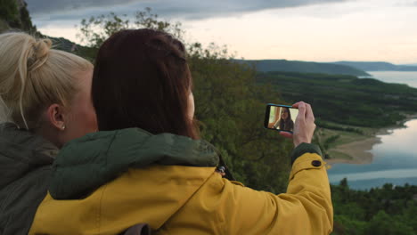 two friends taking a selfie in the mountains overlooking a lake