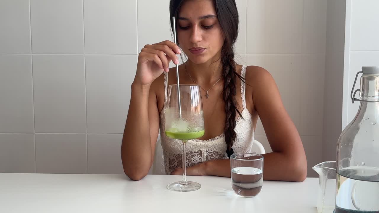Giovane donna che mescola una bevanda verde salutare su un tavolo bianco.