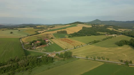 aerial images of tuscany in italy cultivated fields summer, small farm with mountains in the background colorful sown fields