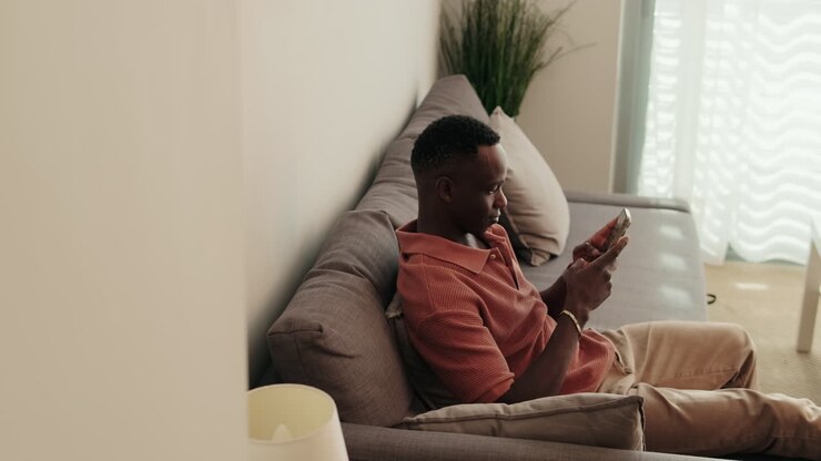 Giovane uomo di colore rilassato sul divano che usa lo smartphone a casa