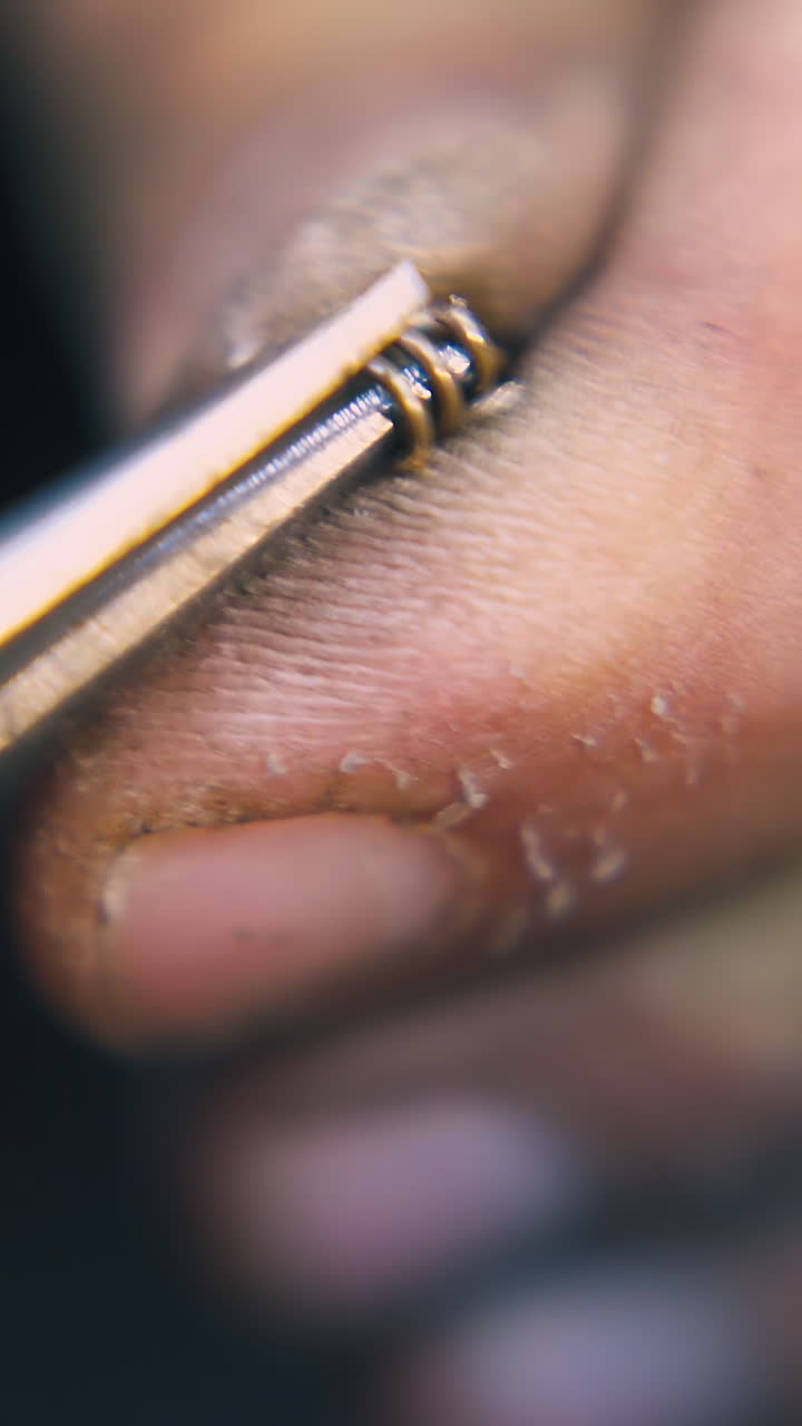 CU: skilled goldsmith connects little links of decorative chain with special nippers on black background extreme closeup