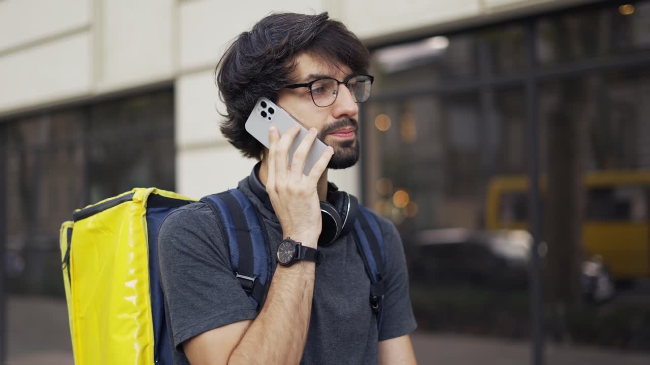 hombre de entrega con mochila amarilla llamando a un cliente en la calle