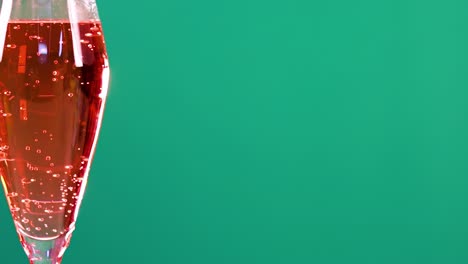 a rose sparkling wine cocktail is garnished against a vibrant green background, highlighting the drink's effervescence and elegance