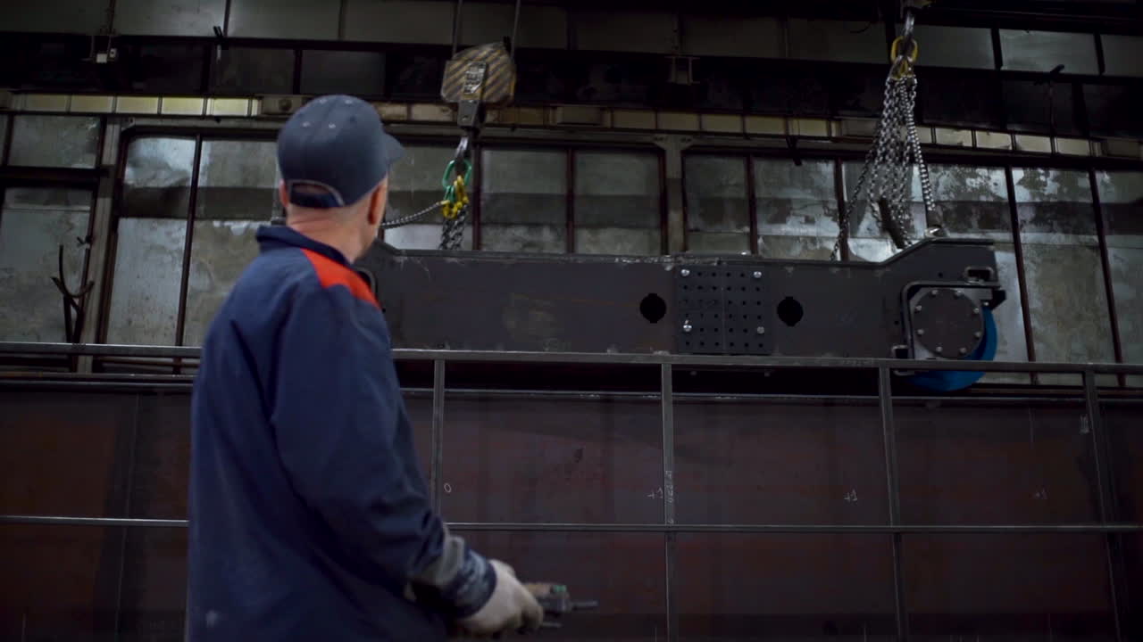 Industrial worker observing heavy machinery lifting a component in a factory