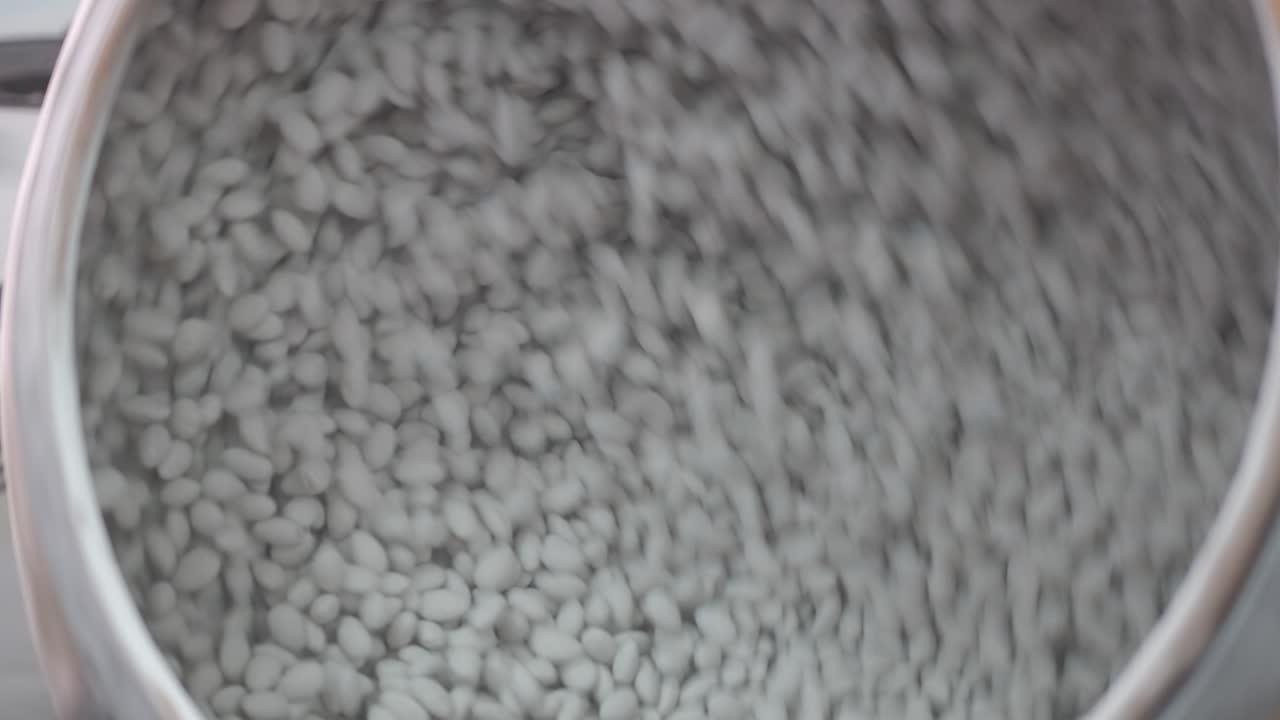 작업자가 공장에서 설탕을 입힌 아몬드가 담긴 큰 회전 통에 손을 뻗습니다.