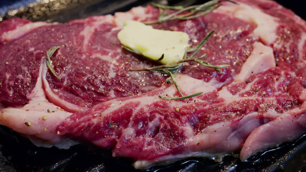Burro che si scioglie su una bistecca condita che cuoce su una padella griglia calda con rosmarino
