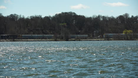 freight trains along tree-lined shoreline of burlington bay. hamilton harbour in ontario, canada. wide static shot
