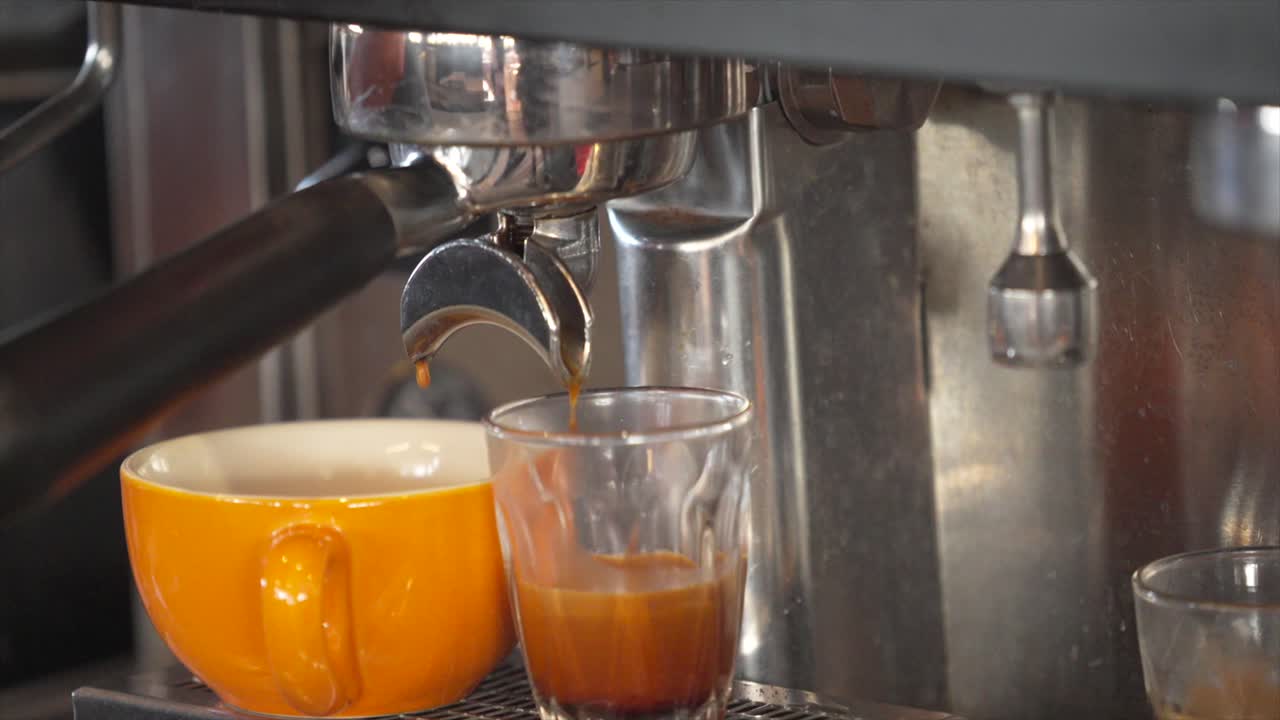 Cuplikan jarak dekat espresso yang mengalir ke dalam gelas dan cangkir dari mesin kopi.