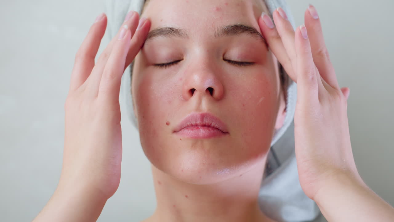 Portrait view of young woman massaging face with skincare, enjoying gentle self-care routine. Relaxed expression, soft motion emphasizing soothing and rejuvenating facial treatment