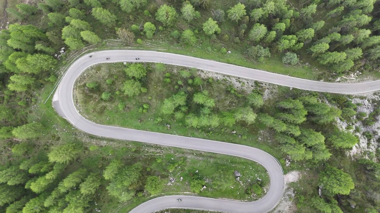 Affascinante prospettiva aerea 4K con drone che guarda direttamente in basso mentre le auto si fanno strada lungo le iconiche strade tortuose incise nelle Dolomiti, Italia settentrionale.