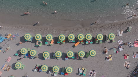 top down aerial footage of the waves of the sea rolling up to the beach with tourists and beach umbrellas