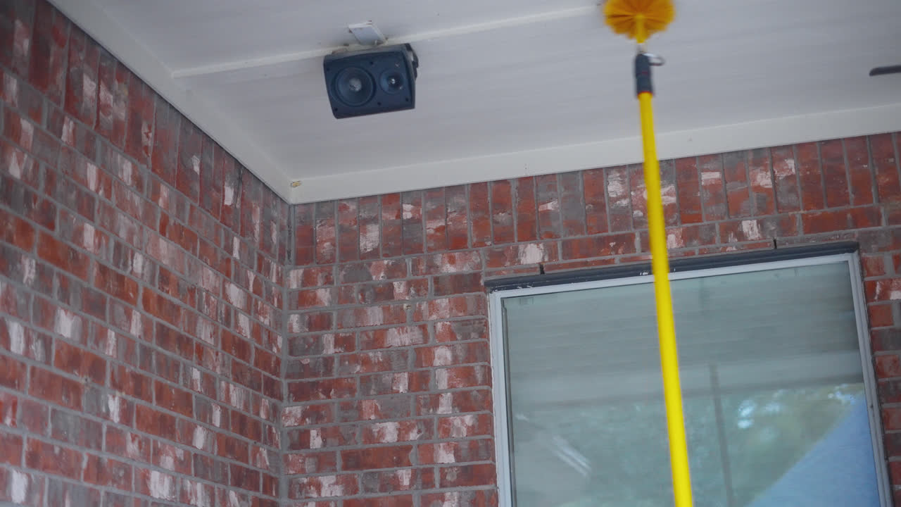 Cleaning exterior security camera using long handled duster pole near brick wall