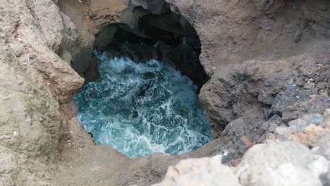 ocean waves crashing and splashing beneath a hole in the volcanic coastal rocks of los hervideros in lanzarote