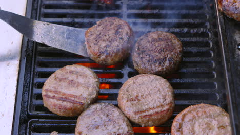 overhead view of meat beef burgers being cooked on hot bbq grill with flames below and chef flipping hamburgers. barbecue summer cooking food.