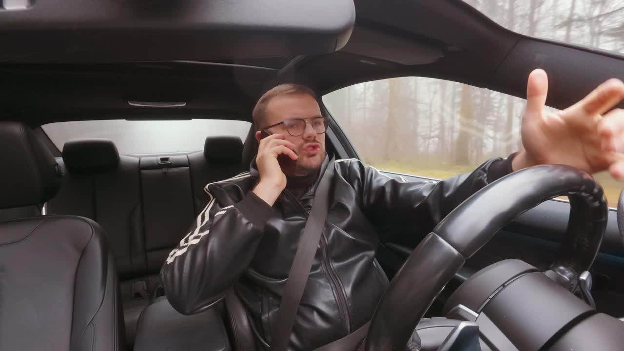 Foto dall’interno di un’auto di un uomo che tiene un telefono all’orecchio mentre guida, che evidenzia la guida distratta, i rischi per la sicurezza stradale e la condotta pericolosa al volante