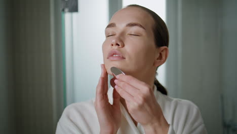 woman doing gua sha lifting treatment closeup. serene girl massage face at home