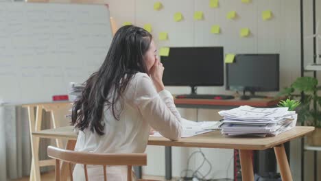 vista posterior de una mujer asiática bostezando antes de dormir mientras trabaja duro con documentos en la oficina