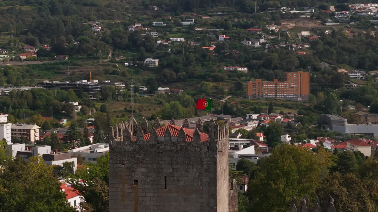 Portuguese flag waving above Guimarães Castle parallax revealing cityscape and surrounding hills