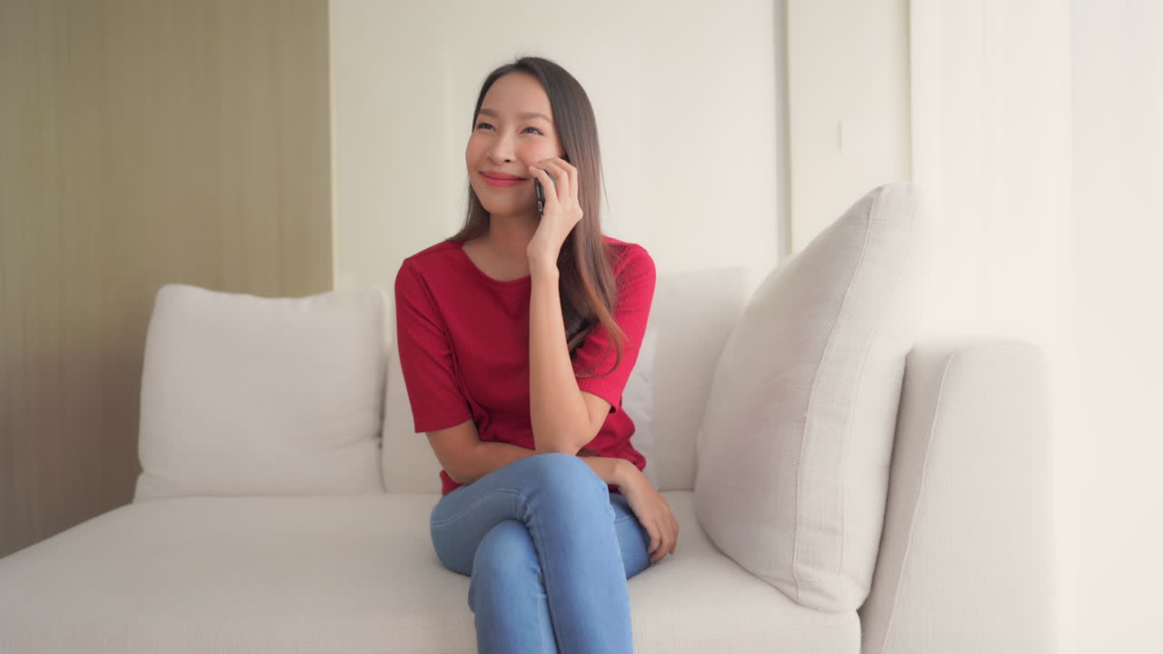 A young woman sitting on a couch while talking on her cell phone
