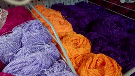 Colorful skeins of yarn in red, purple, orange, and lilac neatly displayed on store shelf