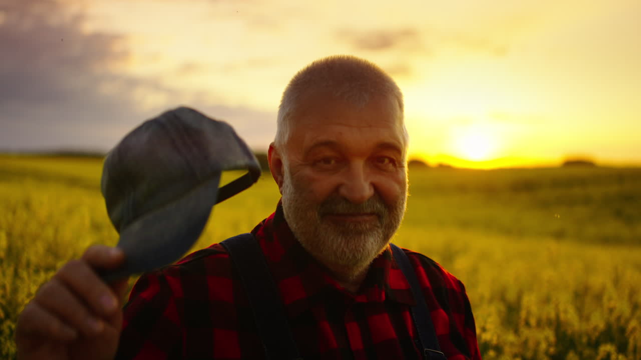 Glad ældre landmand smiler på en gylden mark ved solnedgang