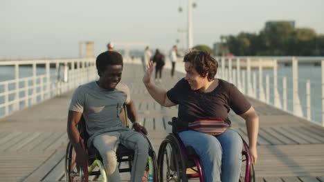 happy friends using wheelchairs walking on bridge