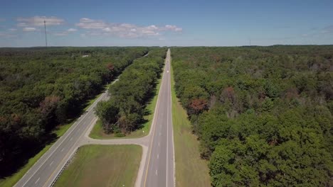 clip of a scenic empty rural american asphalt highway in michigan, america with sunny blue sky in the summer, with green trees all around