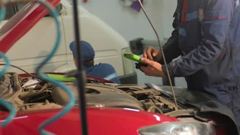 el electricista o mecánico de servicio de automóviles utiliza una tableta con software de diagnóstico interactivo futurista. inspeccionando el vehículo para encontrar componentes rotos en el compartimento del motor del automóvil moderno