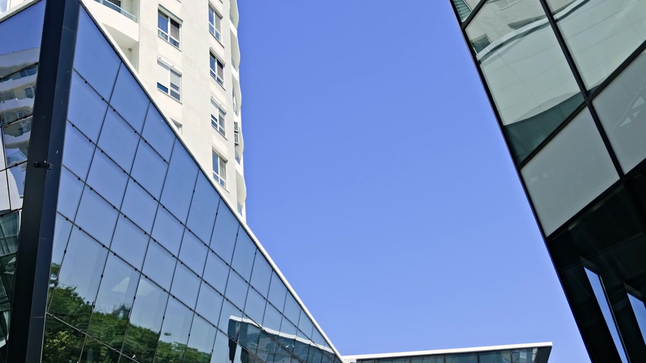 Edificio con esterno in vetro riflette il cielo blu e gli alberi vicini in un'area urbana di giorno, con tempo sereno e il sole che splende