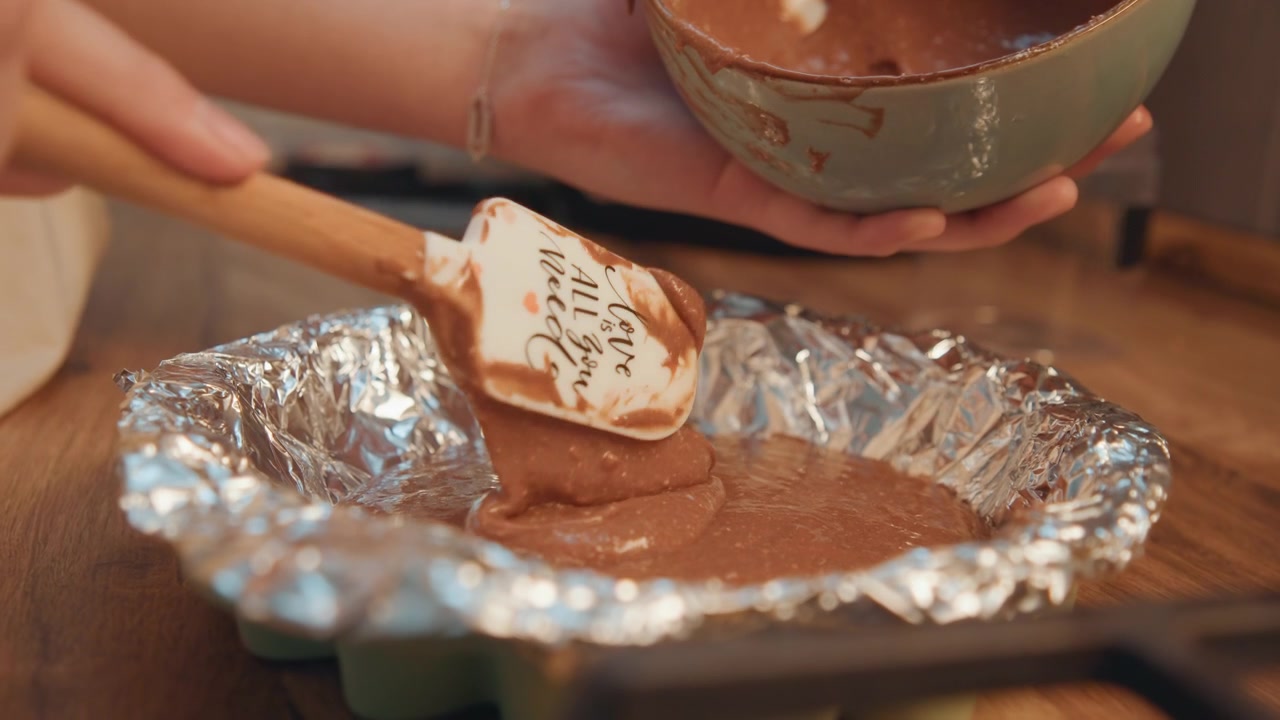 Impasto versato. Mani che trasferiscono l'impasto dolce in una teglia. Miscela di cioccolato versata con cura in una pirofila. Preparazione alla cottura riempiendo una teglia con un delizioso impasto al cioccolato in una cucina calda.