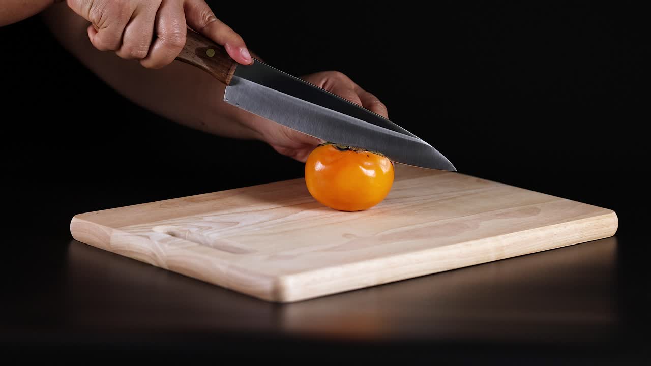 manos cortando cuidadosamente un fruto maduro de caqui