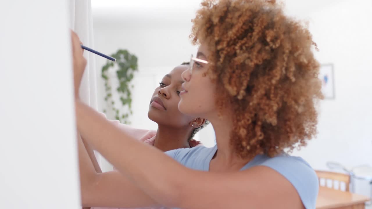 Happy diverse female lesbian couple taking notes on wall in slow motion