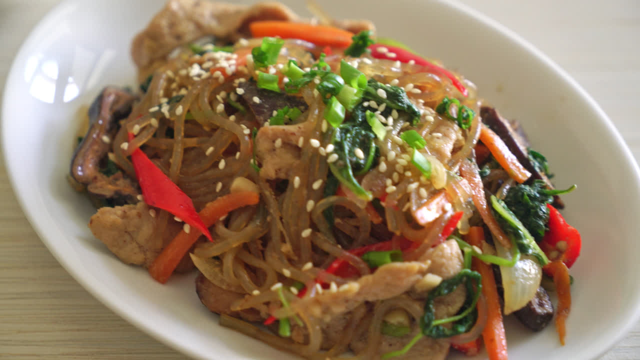 japchae o fideos vermicelli coreanos salteados con verduras y cerdo cubiertos con sésamo blanco - estilo de comida tradicional coreana