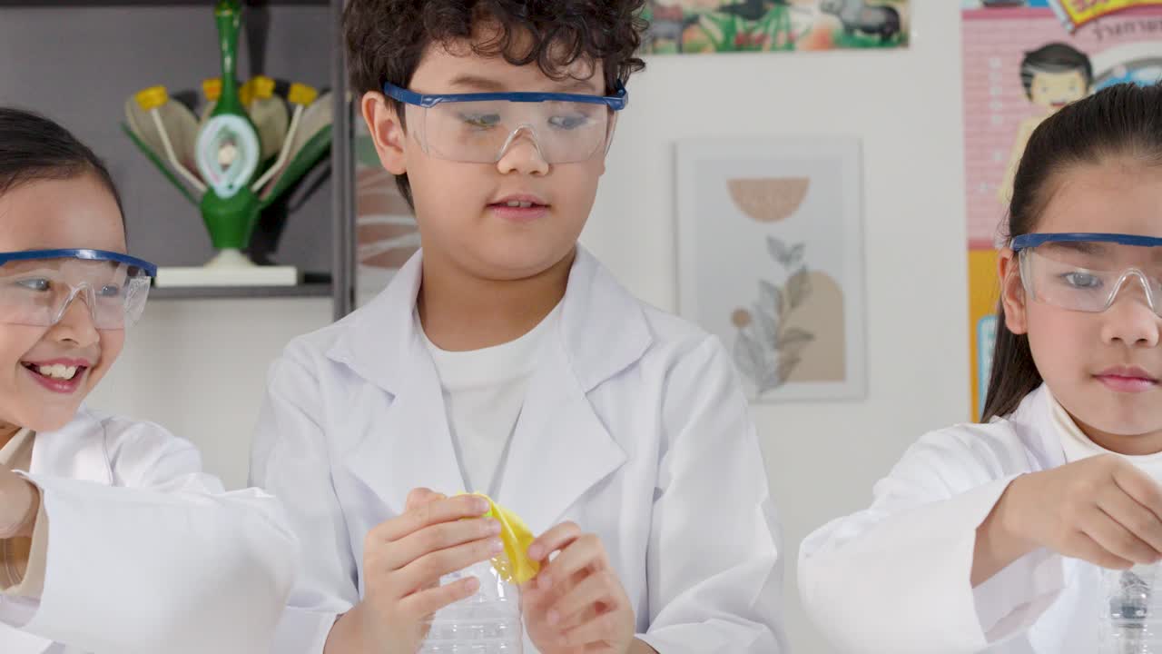 Siswa Thailand mengenakan kacamata pengaman dan jas lab saat memasang balon ke botol plastik.