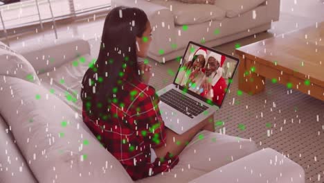 Animation-of-snow-falling-over-mixed-race-woman-on-laptop-video-call-with-family-at-christmas