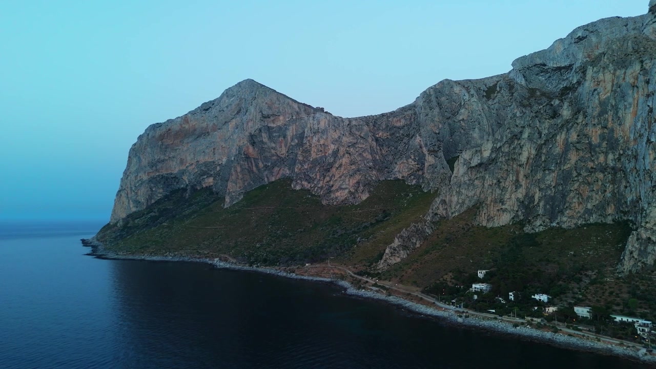 Filmatisk luftfoto af fiskerlandsbyen Sferracavallo og de massive bjerge i Capo Gallo naturreservat i skumringen i Palermo, Italien.