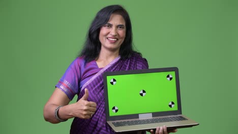 mature happy beautiful indian woman showing laptop and giving thumbs up
