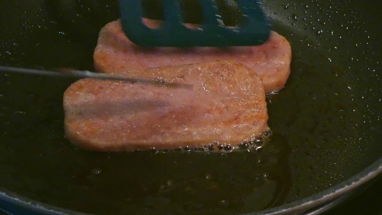 Spam sizzling in a frying pan and being flipped over to cook High cholesterol breakfast