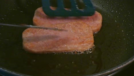 spam sizzling in a frying pan and being flipped over to cook high cholesterol breakfast