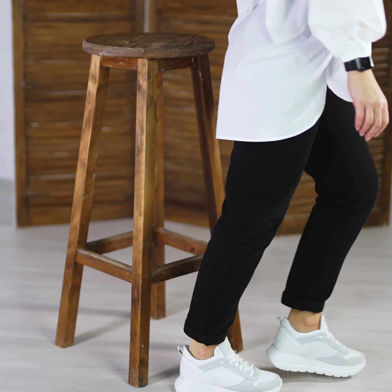 Woman sits on a high stool waving her feet in white sneakers. Model jumps off the tabouret and walks away in comfortable footwear